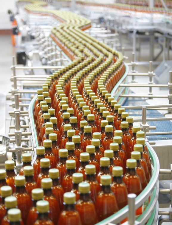 Das Bild zeigt eine Produktionslinie, auf der viele Flaschen einer roten Flüssigkeit abgefüllt und verpackt werden. Es sieht nach einem industriellen Herstellungsprozess für ein Getränk- oder Lebensmittelprodukt aus.