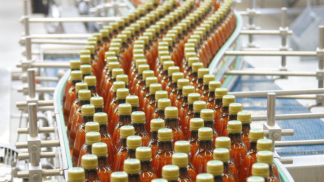  Das Bild zeigt eine Produktionslinie, auf der viele Flaschen einer roten Flüssigkeit abgefüllt und verpackt werden. Es sieht nach einem industriellen Herstellungsprozess für ein Getränk- oder Lebensmittelprodukt aus.