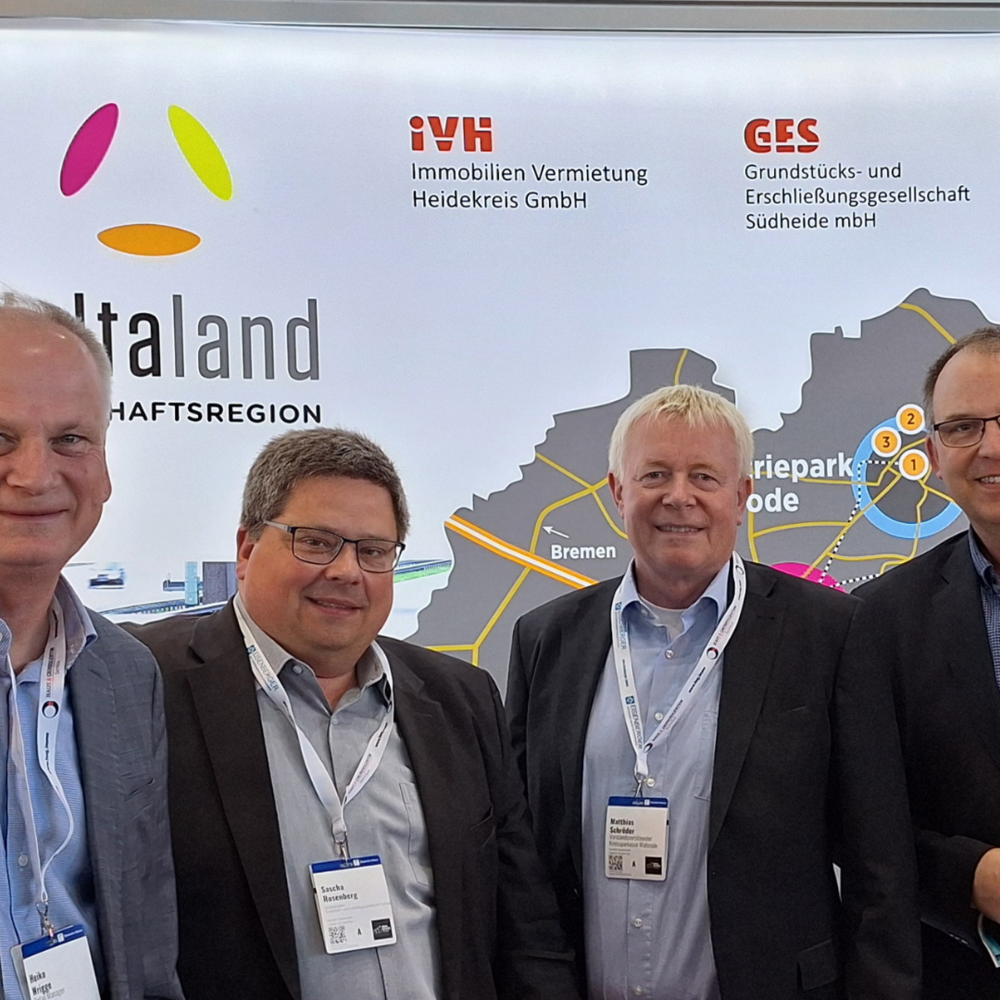 Das Bild zeigt vier Männer in Businesskleidung, die gemeinsam vor einem Messestand der Wirtschaftsregion „Deltaland“ stehen. Im Hintergrund sind Logos von regionalen Unternehmen und Institutionen wie der Kreissparkasse Walsrode sowie eine Karte mit den Standorten der Region zu sehen.