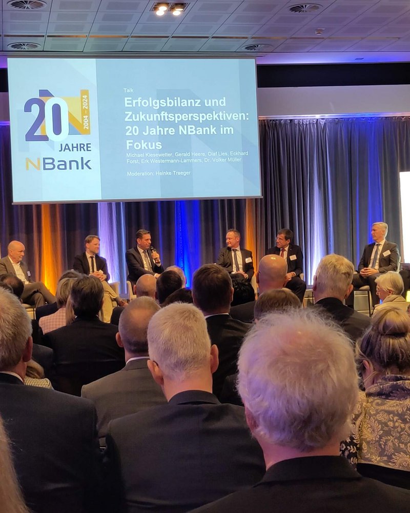 Feier zum 20-jährigen Jubiläum der NBank mit einer Podiumsdiskussion im Alten Rathaus von Hannover, aufgenommen am 12. März 2024. Auf der Bühne diskutieren sechs führende Persönlichkeiten der NBank und der niedersächsischen Wirtschafts- und Politiklandschaft, geleitet von der Moderatorin Heinke Traeger. Im Hintergrund ist ein Banner mit der Aufschrift "20 Jahre NBank" zu erkennen, das Publikum besteht aus hochrangigen Gästen. Foto © Deltaland.