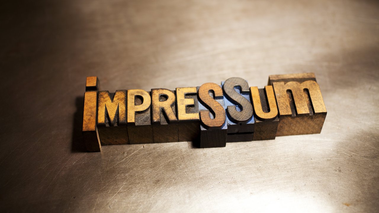  Das Bild zeigt das Wort "Impressum", das in großen, rustikalen Buchstaben auf einer Metalloberfläche geschrieben ist. Die Buchstaben sind aus Holz und in einem Retro-Stil gestaltet. Jeder Buchstabe ist in einen Holzblock geschnitzt und diese Blöcke sind nebeneinander angeordnet, um das Wort zu bilden.