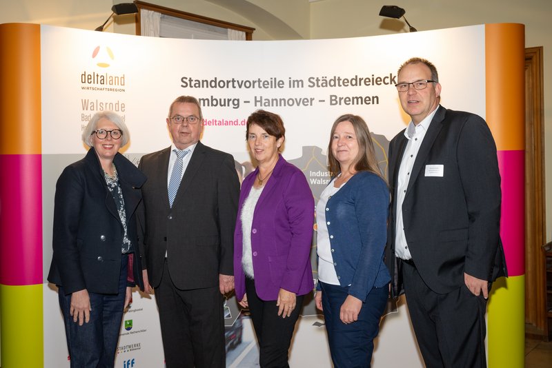 Das Bild zeigt eine Gruppe von fünf Personen, die in formeller Kleidung vor einem großen Banner stehen, das Informationen über Standortvorteile in der Region Walsrode, Hannover und Bremen präsentiert. Die Atmosphäre wirkt professionell und freundlich, was auf eine Veranstaltung hindeutet.