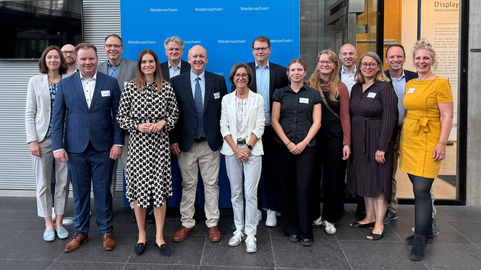 Vor einem blauen Hintergrund mit dem Logo der Landesvertretung Niedersachsen steht eine Gruppe von Menschen in Businesskleidung und lächelt in die Kamera. Das Foto wirkt offiziell und wurde vermutlich im Rahmen eines parlamentarischen Frühstücks oder einer politischen Veranstaltung aufgenommen.