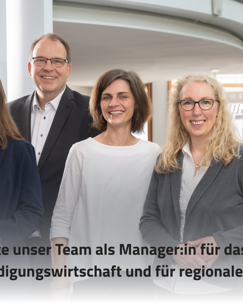 Das Bild zeigt vier Personen in einem modernen Büroumfeld, die freundlich in die Kamera lächeln. Im Vordergrund steht der Text "Verstärke unser Team als Manager:in für das Cluster Rüstungs-/Verteidigungswirtschaft und für regionale Projekte [m/w/d]".